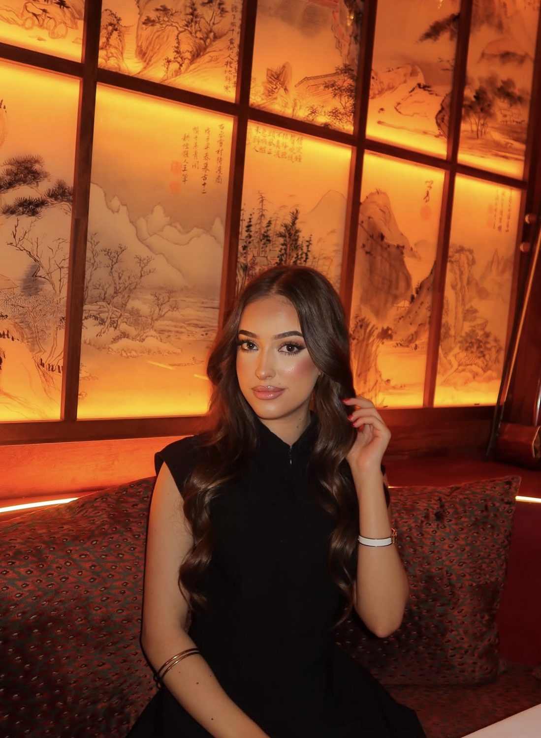 Lia with long glossy waves, seated in warm amber light